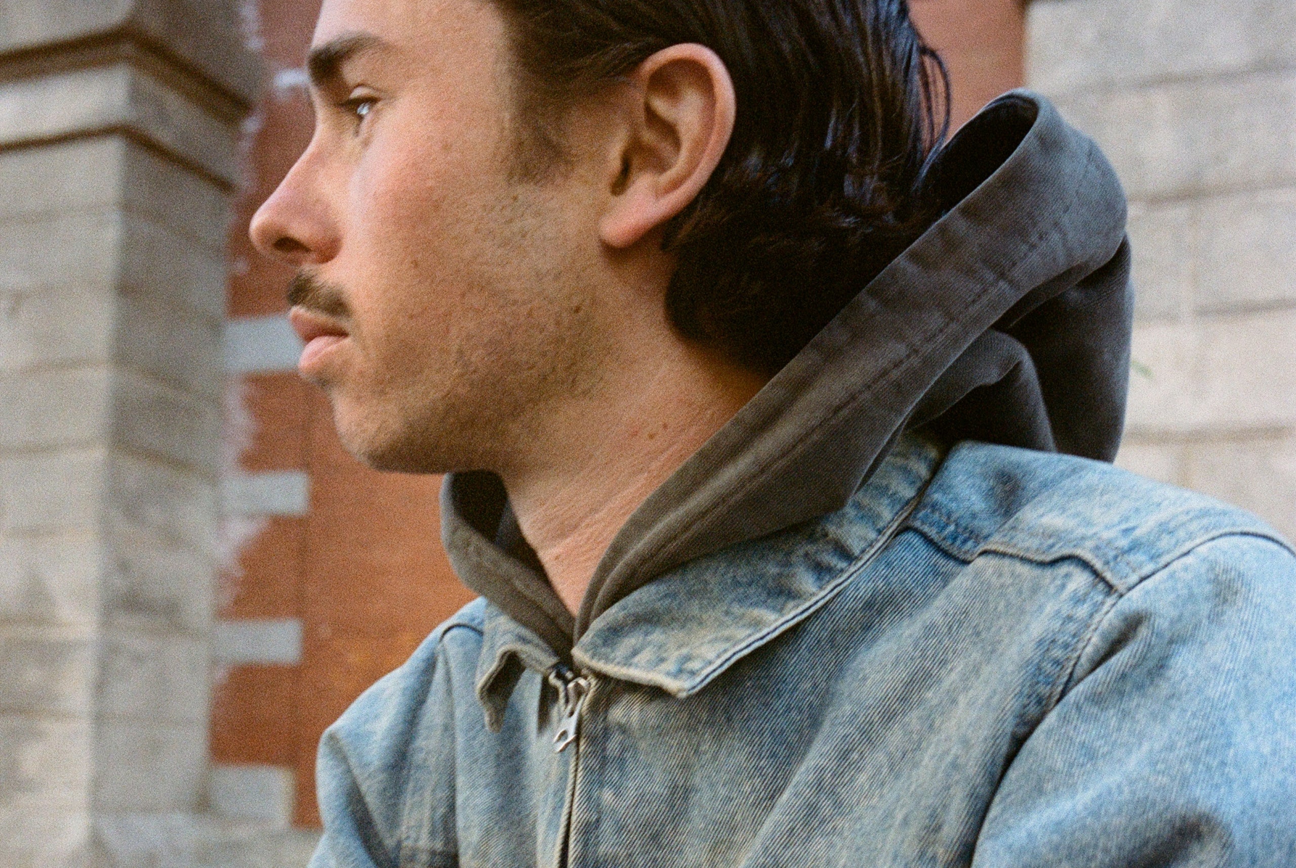 Man wearing a denim jacket with a hood in front of a brick wall