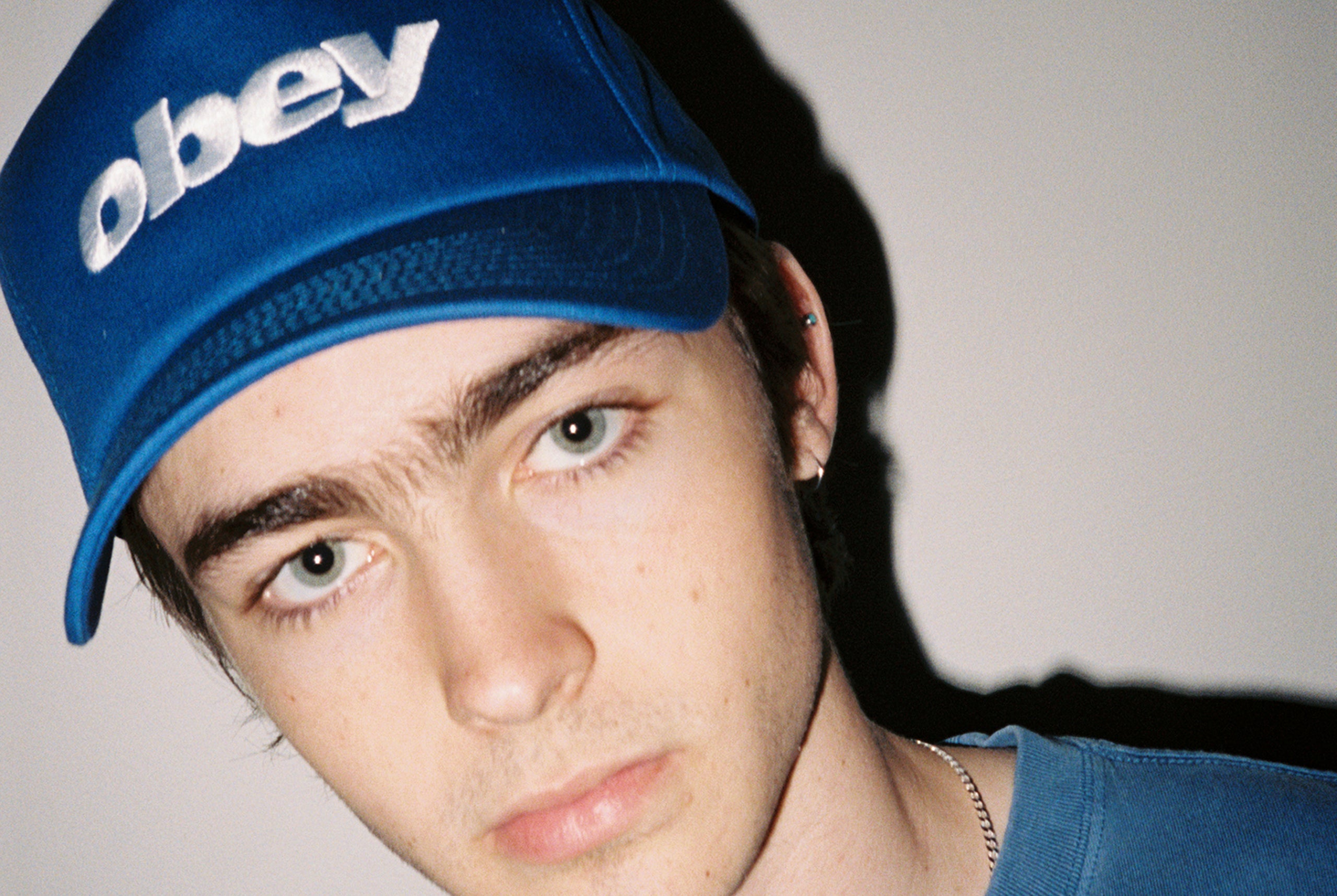 Person wearing a blue 'obey' cap against a plain background