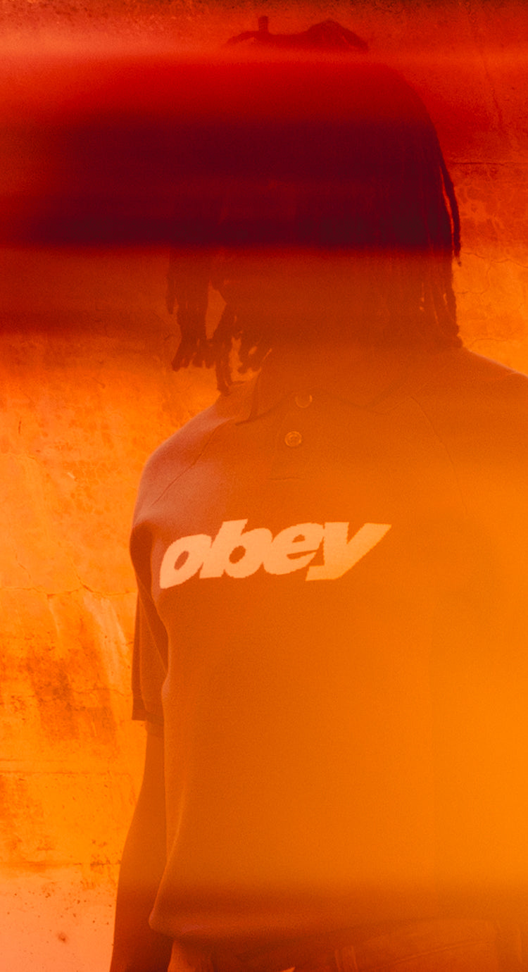 Person wearing a hoodie with 'obey' logo in an orange-tinted setting