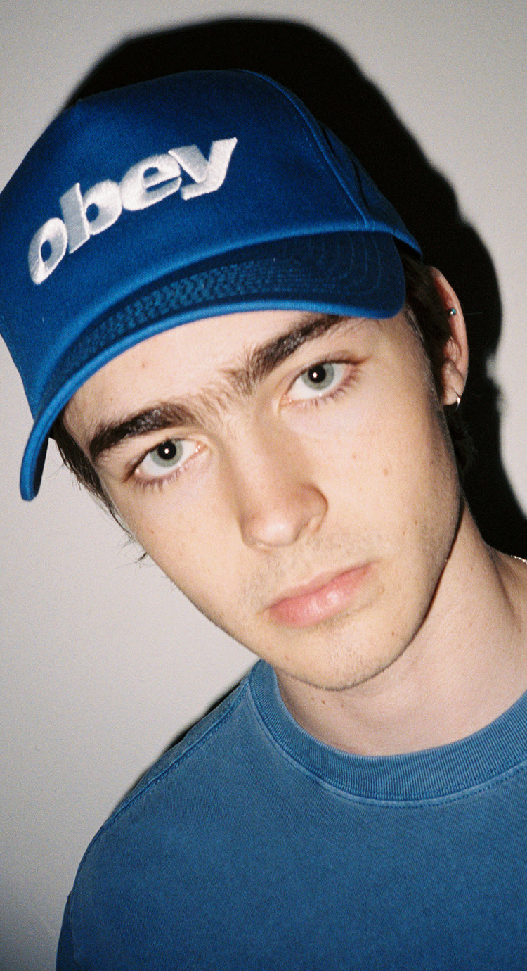 Person wearing a blue 'obey' cap against a neutral background